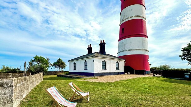 A lighthouse with a white and red exterior, a white building adjacent to it, and two striped beach chairs on the grass. - 2 bedroom accommodation in Happisburgh, near Cromer (Happisburgh, near Cromer)