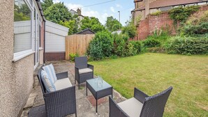 A patio with wicker furniture and a glass table, surrounded by a grassy lawn and a wooden fence. - 3 bedroom accommodation in Morecambe (Morecambe)