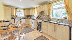 A modern kitchen with wooden cabinets, a dining area with a table and chairs, and a window with curtains. - 3 bedroom accommodation in Morecambe (Morecambe)