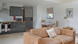 A modern kitchen with grey cabinets, a microwave, and a red fire extinguisher. There is a beige sofa with a floral pillow and a small table with a lamp. - 1 bedroom accommodation in near Comrie and Crieff (near Comrie and Crieff)