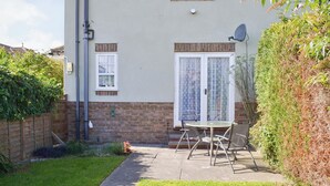 Une maison à deux étages avec une façade en briques, une antenne parabolique et un petit patio équipé d’une table et de chaises.