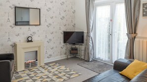 Un salon avec un canapé, une cheminée, un téléviseur et un papier peint à motifs.
