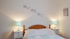 Un lit bien fait, recouvert d’une courtepointe, deux tables de chevet avec des lampes et des autocollants décoratifs aux murs avec des messages inspirants.