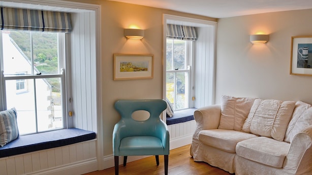 A room with a blue chair, a white sofa, and two windows with curtains. - 2 bedroom accommodation in Port Isaac (Port Isaac)