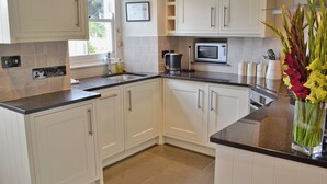 A modern kitchen with white cabinets, a black countertop, a microwave, and a coffee maker. - 2 bedroom accommodation in Port Isaac (Port Isaac)