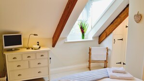A bedroom with a bed, a dresser, a television, a window with a view of greenery, and a wooden ceiling beam. - 2 bedroom accommodation in Port Isaac (Port Isaac)