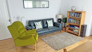 A living room with a sofa, green armchair, wooden coffee table, bookshelf, and a mirror on the wall.