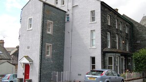 A two-story building with a red door, stone facade, and a parked car in front.