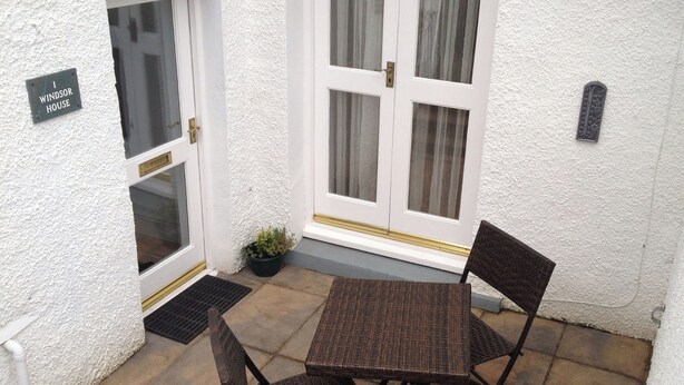 A small patio with a table and chairs, a potted plant, and a sign reading 'Windsor House.'