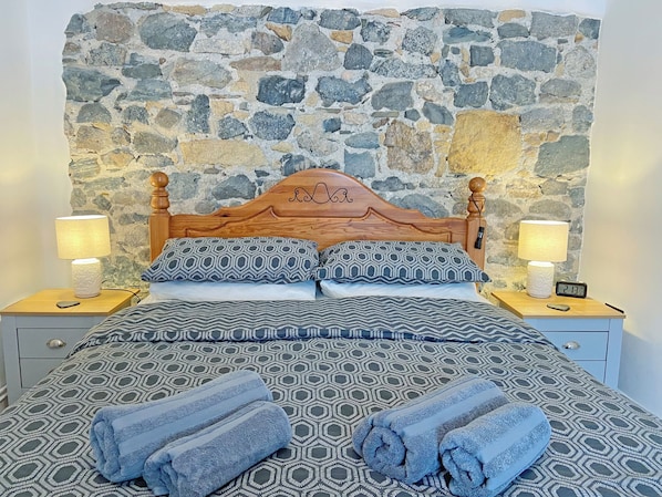 Ein Bett mit gemusterten Bettbezügen, zwei Nachttischlampen, eine digitale Uhr und eine Steinwand im Hintergrund.
