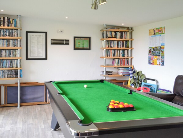 Une table de billard recouverte d’un drap de feutre vert, entourée d’étagères remplies de livres.