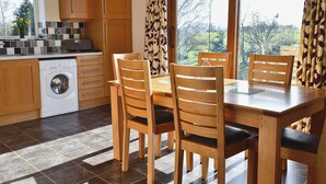Una cocina con armarios de madera, lavadora, mesa de comedor con sillas y una ventana con cortinas.