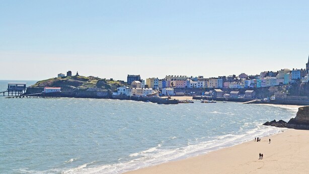 Une ville côtière avec des bâtiments qui bordent la plage, une jetée qui s’avance dans l’eau et une plage de sable où se trouvent quelques personnes.