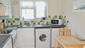 Une cuisine compacte équipée d’un lave-linge, d’un four à micro-ondes et d’un coin repas avec une table et des chaises.