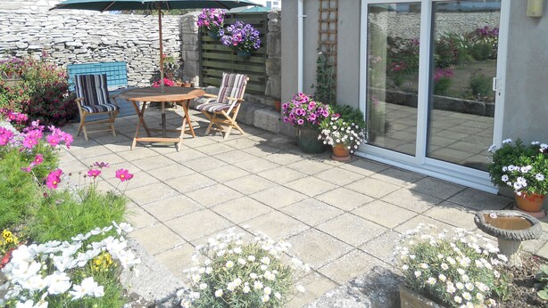 Une terrasse avec une table et des chaises, entourée de plantes et de fleurs en pot.