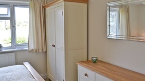 Une chambre à coucher comprenant un lit, une armoire, une commode, un miroir et une fenêtre avec des rideaux.