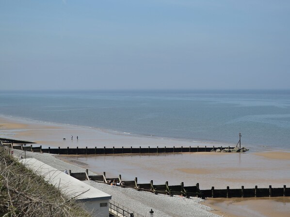 A coastal beach with a concrete walkway and a wooden breakwater.