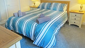 Ein ordentlich bezogenes Bett mit gestreifter Bettwäsche, zwei Nachttischlampen, ein Holznachttisch und ein kleiner Tisch.
