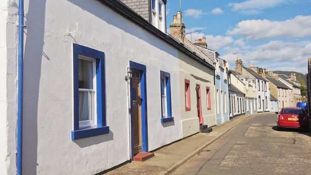 A row of terraced houses with blue window frames and a red car parked on the street.