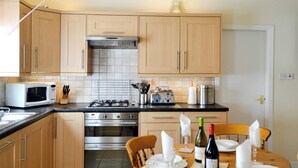 A modern kitchen with wooden cabinets, a gas stove, a microwave, and a dining table set for a meal.