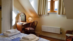 A bedroom with a bed, a desk with a chair, a radiator, and a window with curtains.