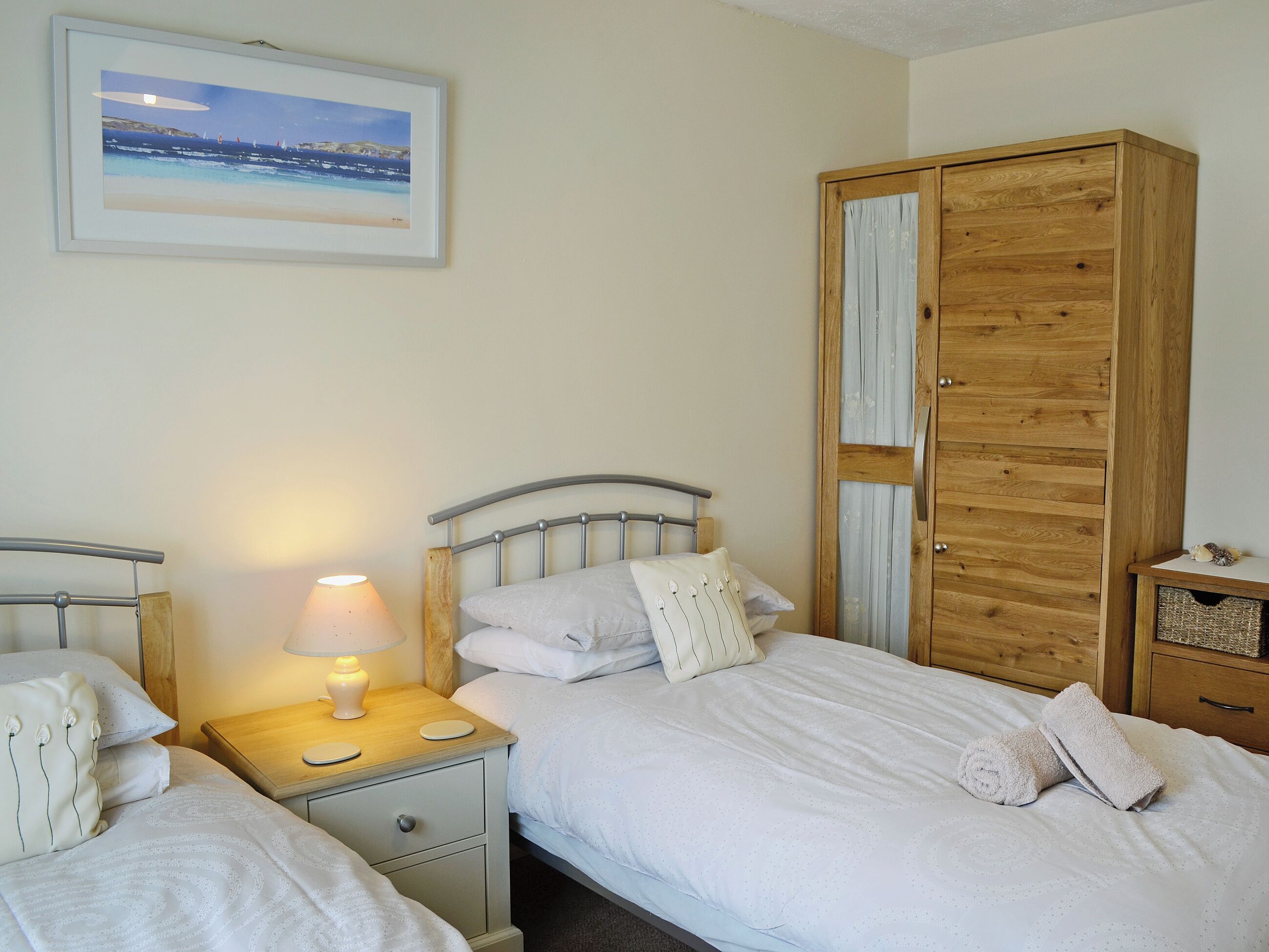 Une chambre avec deux lits, une armoire en bois, une table de chevet avec une lampe et un tableau encadré au mur.