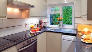 A modern kitchen with white cabinets, a black countertop, a built-in oven, a dishwasher, and a window with a view of greenery.