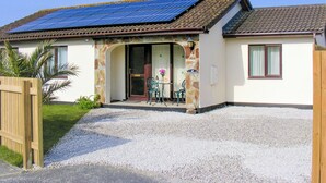 A house with a solar panel roof, a stone facade, a gravel driveway, and a wooden gate.