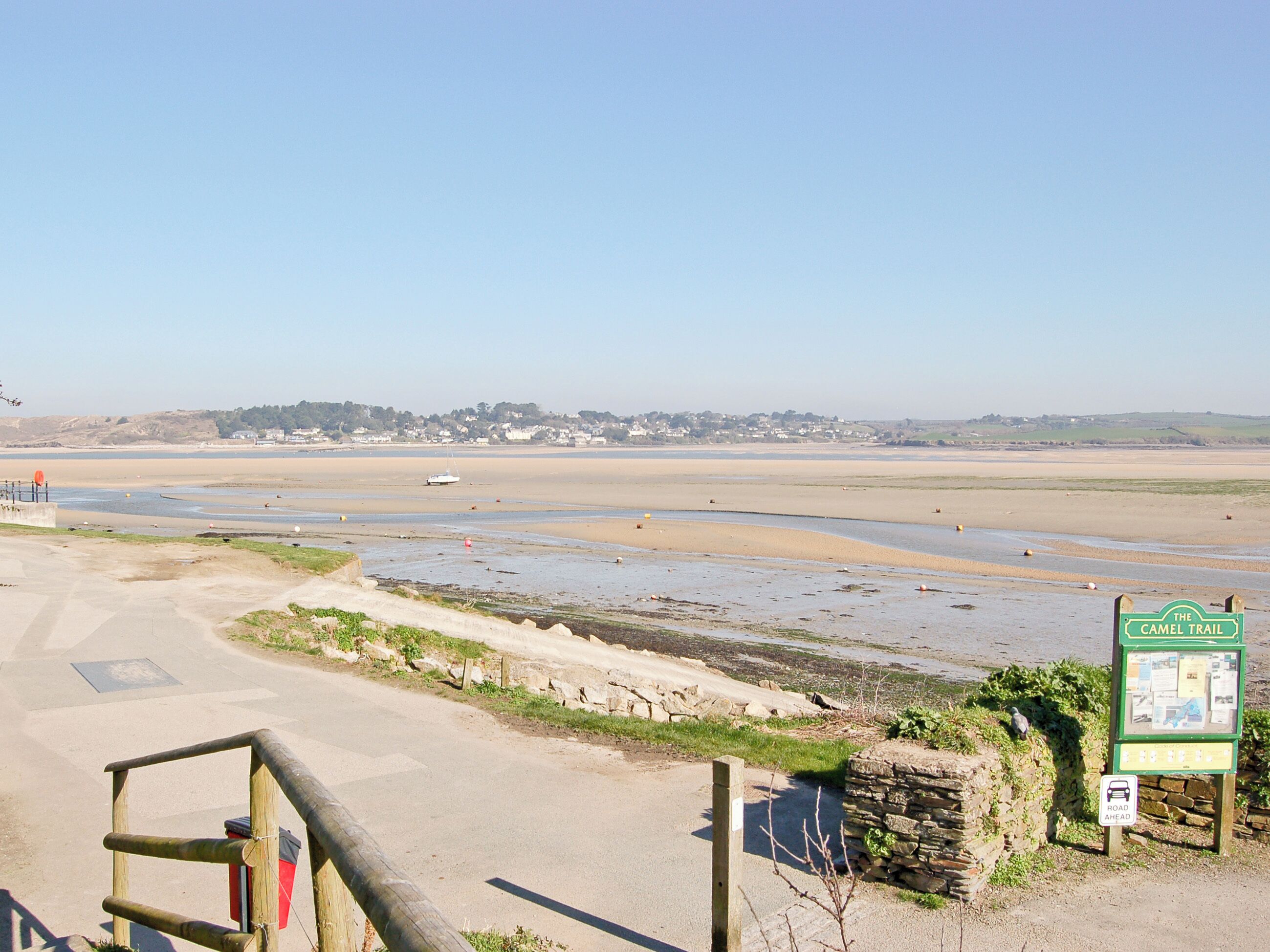 Une route côtière menant à une plage, avec un panneau indiquant « The Camel Trail ».
