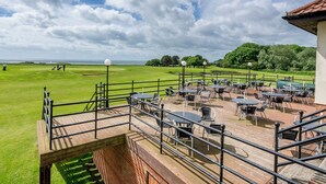 Campo de golf con zona de patio que cuenta con mesas y sillas, con vistas al green.