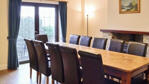 Une salle à manger avec une longue table en bois et des chaises noires, un tableau au mur et une vue par la fenêtre.