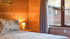 Une chambre dans un chalet en bois, avec un lit, une table de chevet, une lampe et une fenêtre avec des rideaux.