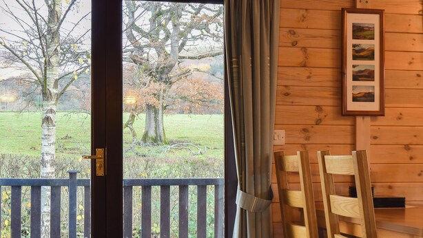 Un intérieur en bois avec une porte donnant sur un balcon, un tableau encadré au mur et une table en bois avec des chaises.