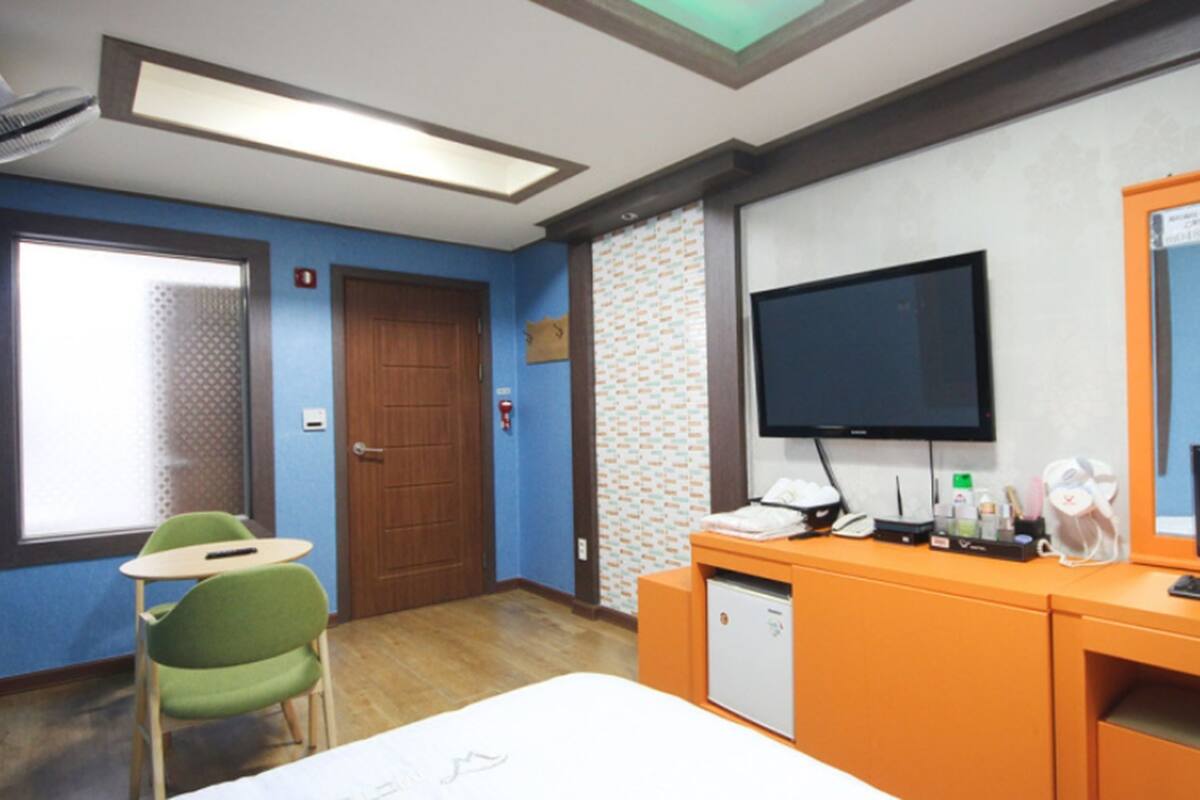 A hotel room with a bed, a desk with a computer, a television, and a small table with a chair.
