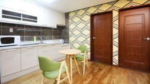 A compact kitchen with white cabinets, a microwave, a sink, and a small dining table with two chairs. - W Motel (Tongyeong)