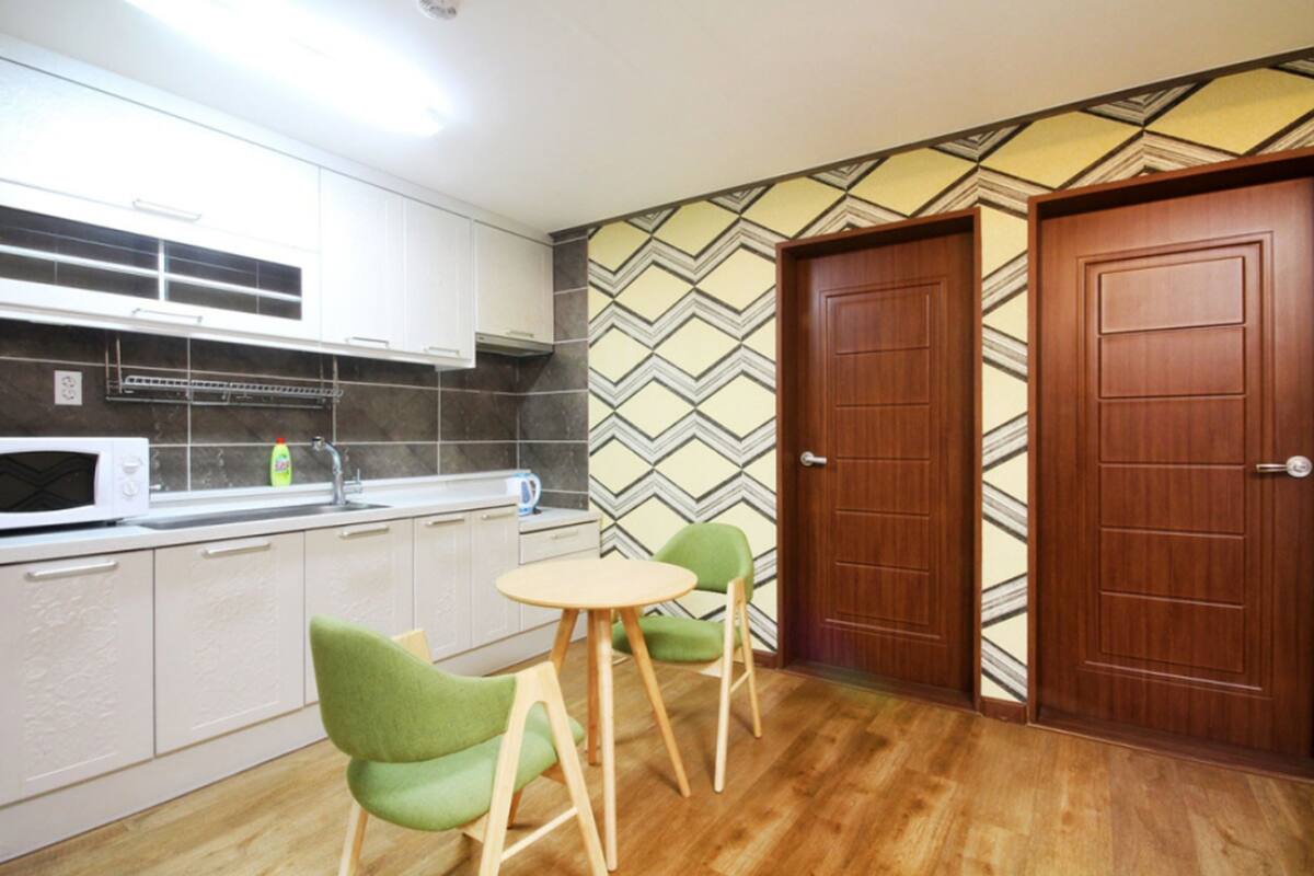 A compact kitchen with white cabinets, a microwave, a sink, and a small dining table with two chairs.