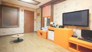 A hotel room with a wooden floor, a television, a small refrigerator, a desk, and a chair. - W Motel (Tongyeong)