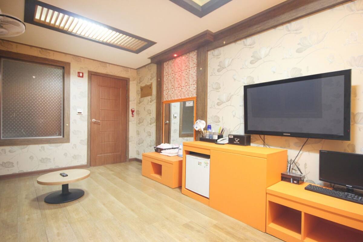 A hotel room with a wooden floor, a television, a small refrigerator, a desk, and a chair.