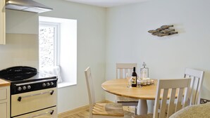 Una cocina con estufa, horno y ventana. Hay una mesa de comedor con sillas y una botella de vino encima.