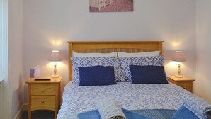 Un dormitorio con una cama de madera, dos mesitas de noche, una lámpara, un cuadro en la pared y una cama bien hecha con ropa de cama azul y blanca.