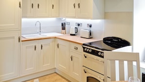 Una cocina moderna con armarios blancos, extractor de acero inoxidable, horno empotrado y encimera con tostadora y cafetera.