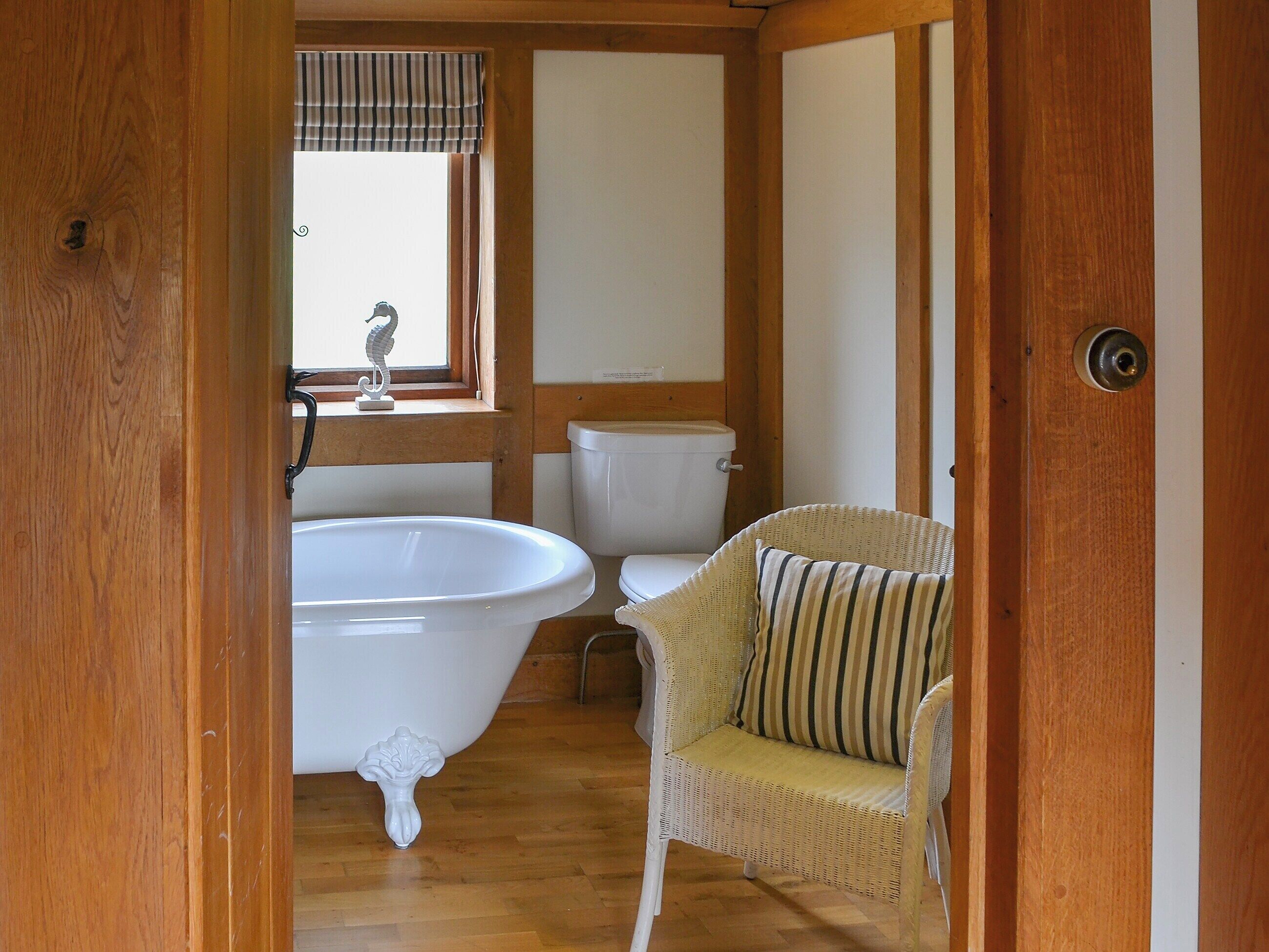 A bathroom with a freestanding bathtub, a toilet, and a wicker chair with a striped cushion.
