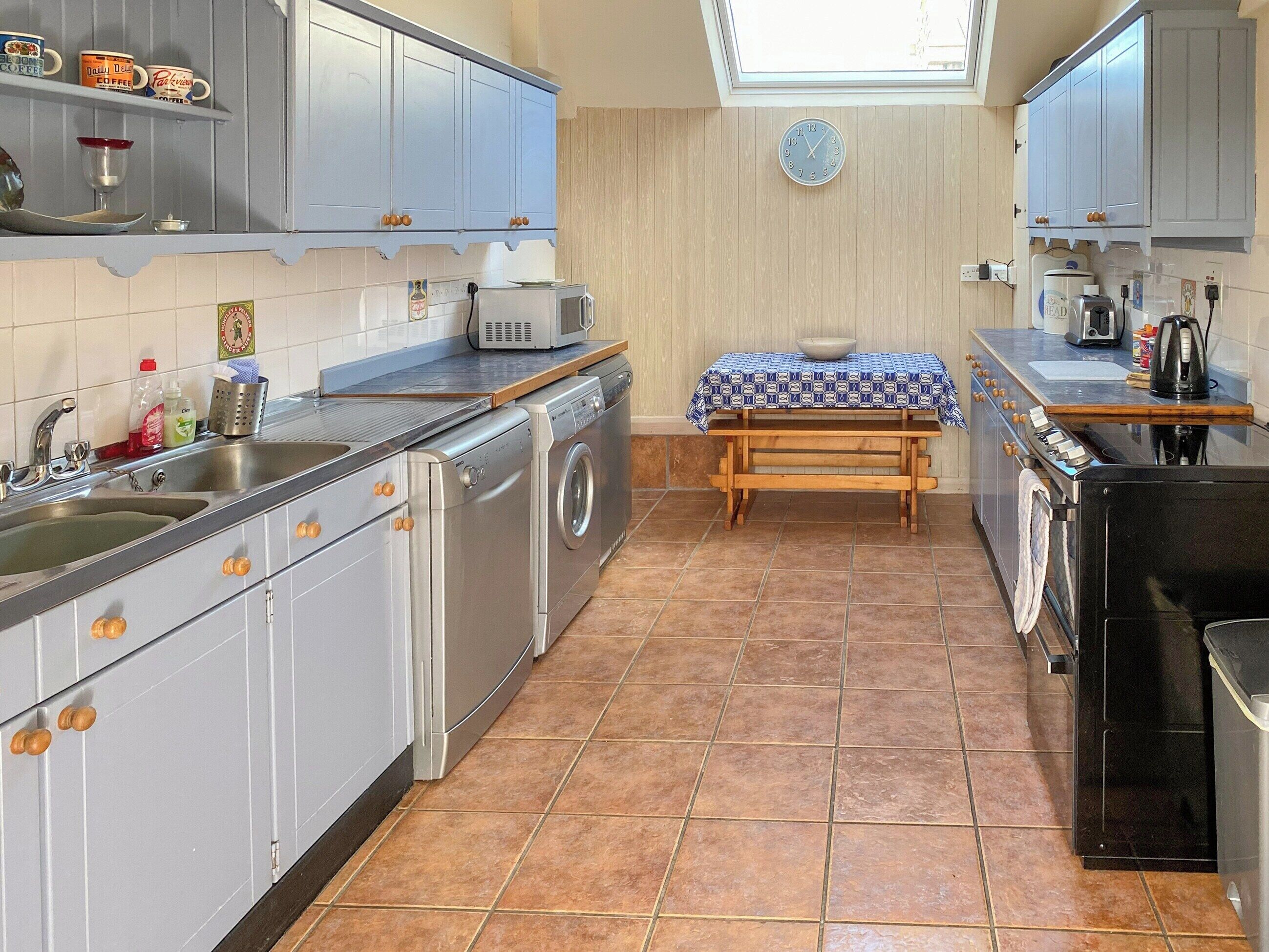 A compact kitchen with grey cabinets, a washing machine, a microwave, and a small table with a blue tablecloth.