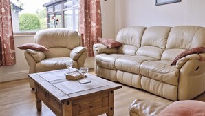 A living room with a beige leather sofa, a wooden coffee table, and a window with curtains. - 3 bedroom accommodation in Bala (Bala)