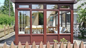 A conservatory with a wooden frame and glass panels, featuring a table and chairs inside. - 3 bedroom accommodation in Bala (Bala)