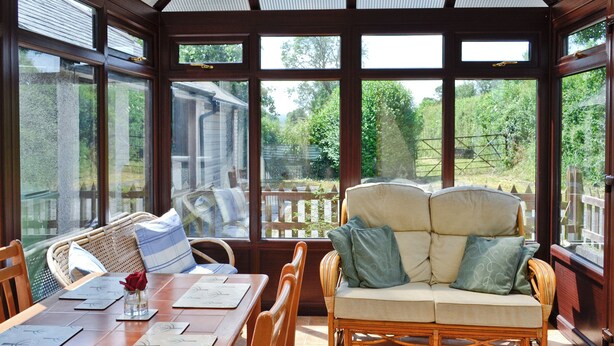 A sunroom with a dining table, wicker sofa, and large windows offering a view of the garden. - 3 bedroom accommodation in Bala (Bala)