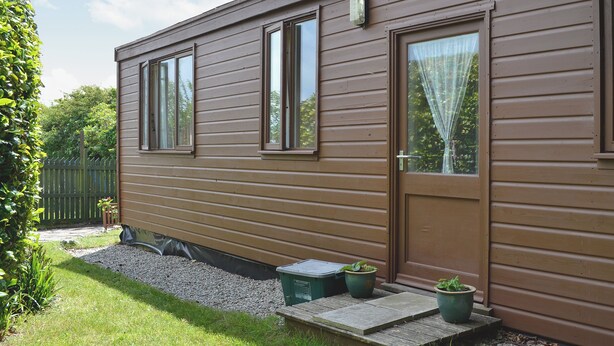 A single-story mobile home with a front door, two windows, and a small porch area with potted plants. - 1 bedroom accommodation in Nancledra, near Penzance (Nancledra, near Penzance)