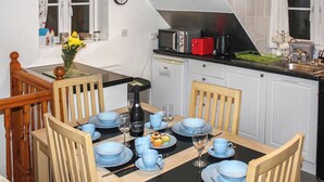 A dining area with a table set for four, a clock on the wall, and a kitchen in the background. - 1 bedroom accommodation in Stalham (Stalham)