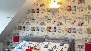A bedroom with a sloped ceiling, a bed with a sailboat-themed duvet, two red lamps, and a wall with a cityscape wallpaper. - 1 bedroom accommodation in Stalham (Stalham)