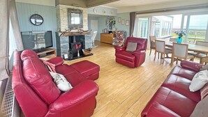 Uma sala de estar com sofás de couro vermelho, lareira, televisão e um espaço de jantar com mesa e cadeiras.